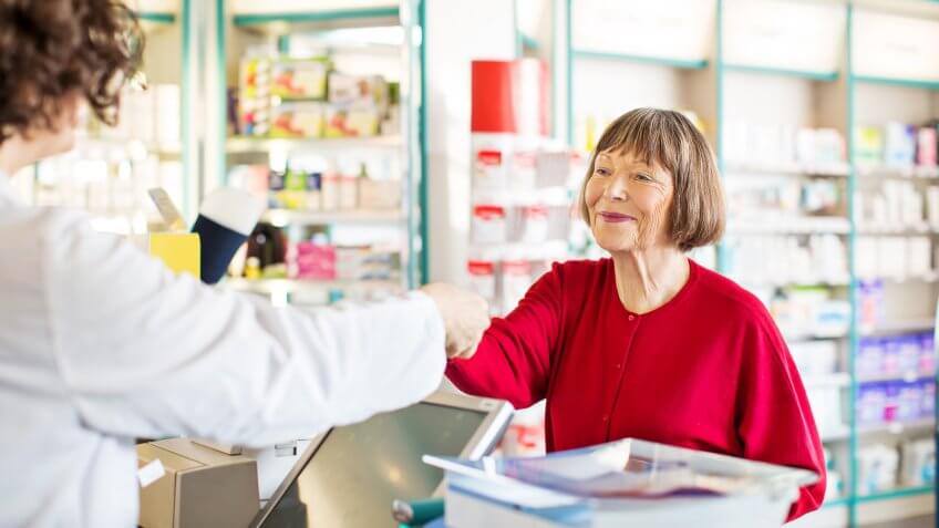 customer standing at chemist counter as pharmacist hands her medication order