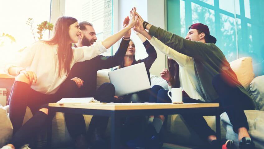 Female and male classmates celebrating pathing math examination, feeling exciting and cheerful , giving high five during informal meeting in friendly atmosphere with modern laptop in coworking space.