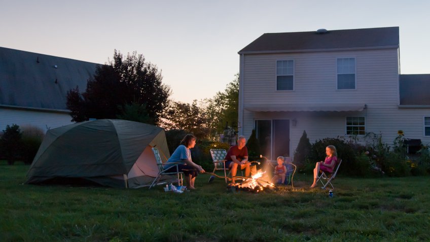 Family with two children, roasting marshmallows over a campfire in their backyard.