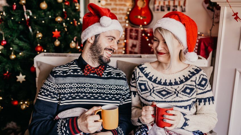 Couple relaxing and drinking tea in front of a Christmas tree.