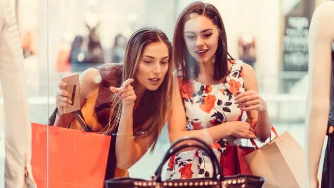 Happy women in the shopping mall looking at the shop window.