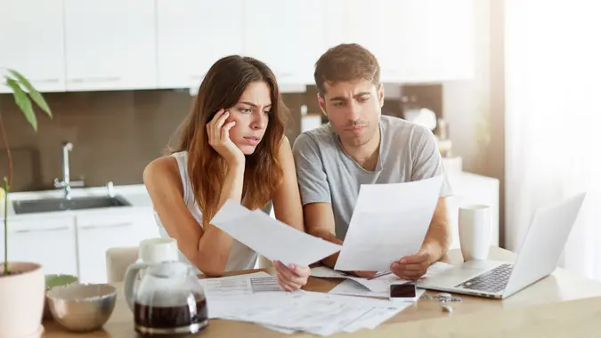 young couple looking at billing statements with concern in a kitchen