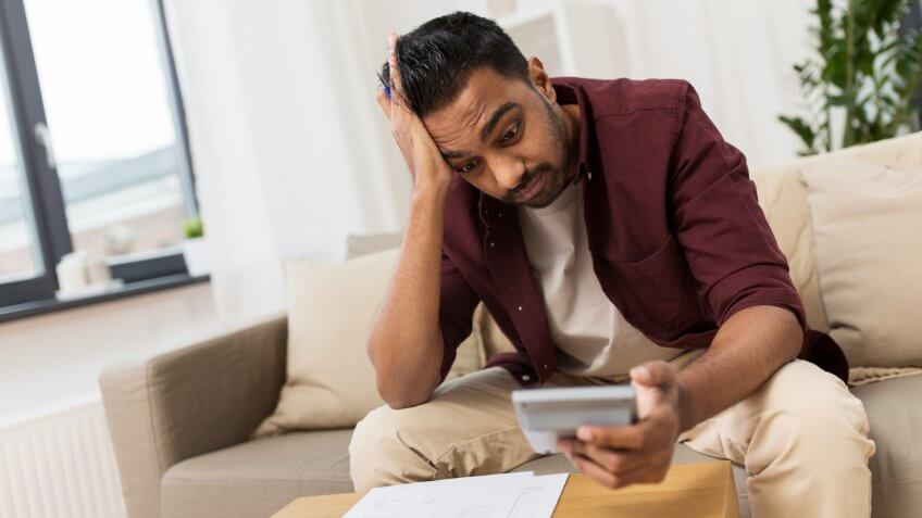business, accounting, finances and people concept - confused man with papers and calculator at home.