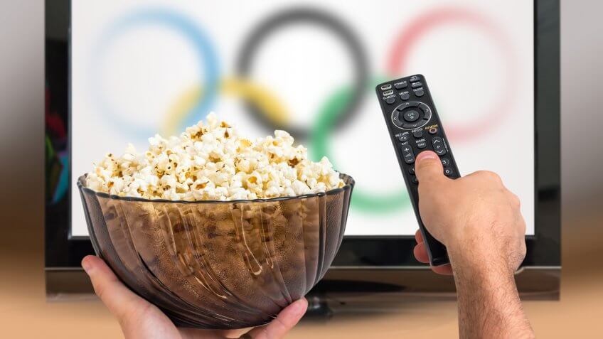 Man is watching sports games on TV and holds remote controller and popcorn in hands.