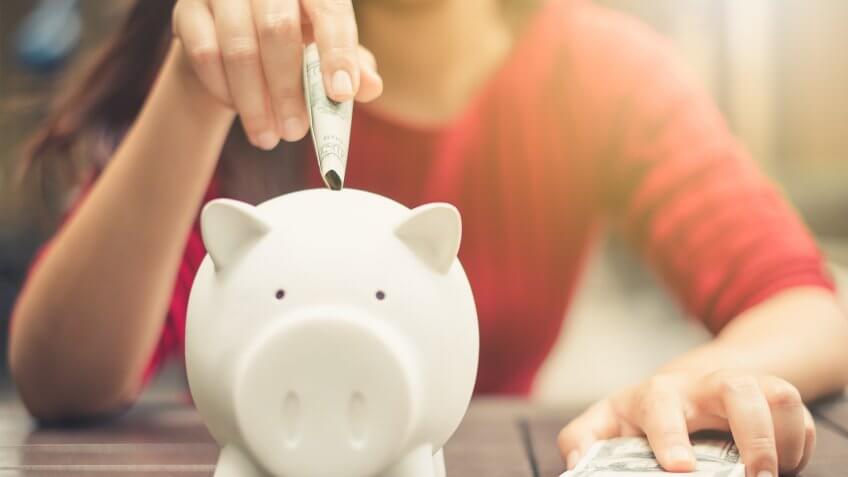 woman inserting cash into a piggy bank