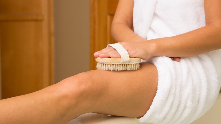Sitting woman's arm holding dry brush to top of outstretched leg.