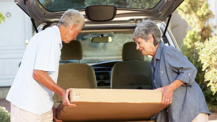 Senior Couple Loading Large Package Into Back Of Car.