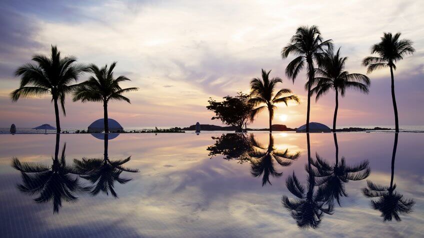 The sun sets over the ocean and an infinity pool in Mexico.