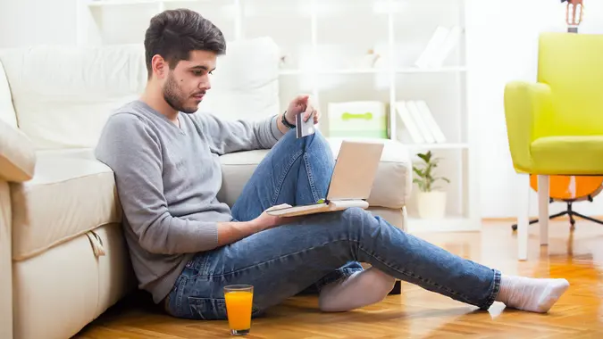 Handsome man holding credit card and using laptop for online shopping - indoors.