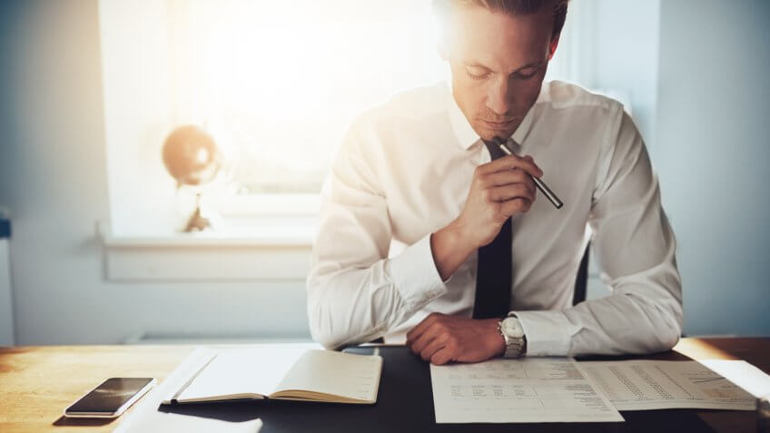 Serious business man working on documents looking concentrated with briefcase and phone on the table.
