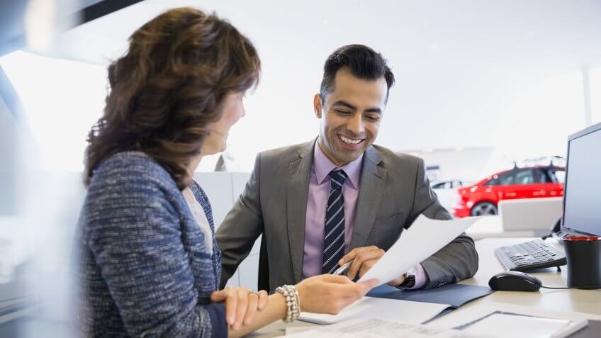 Salesman and woman finalizing paperwork in car dealership.
