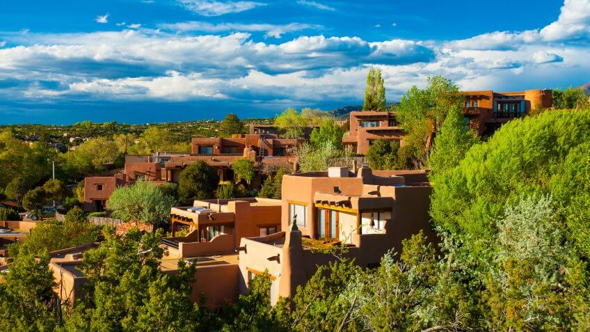 Hillside houses and trees in Santa Fe, New Mexico, with clouds in the background.