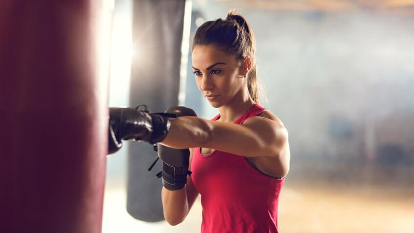 Young muscular build woman punching a bag on a boxing training in a gym.