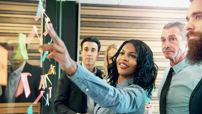 Young smiling black businesswoman at the wall with stickers communicating with her colleagues.