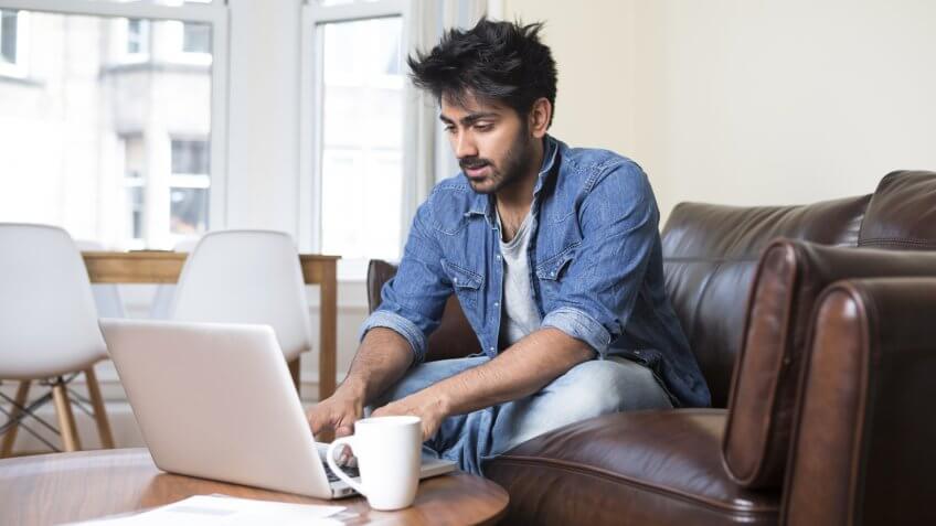 Indian man at home on sofa using a laptop.