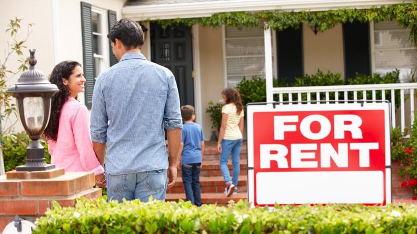 Hispanic family outside home for rent holding hands looking at each other happy.