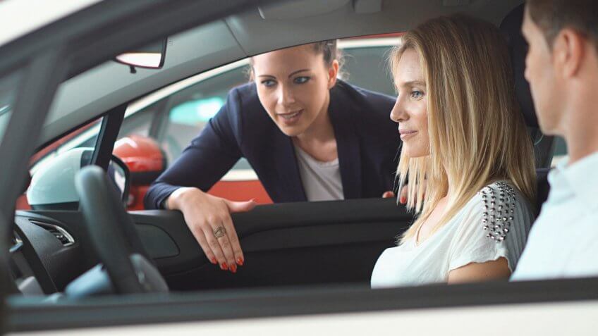 Closeup side view of mid adult couple sitting in a brand new car at a local dealership.