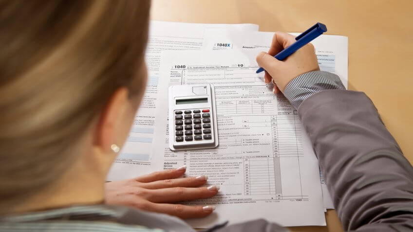 Woman hand filling income tax forms with calculator.