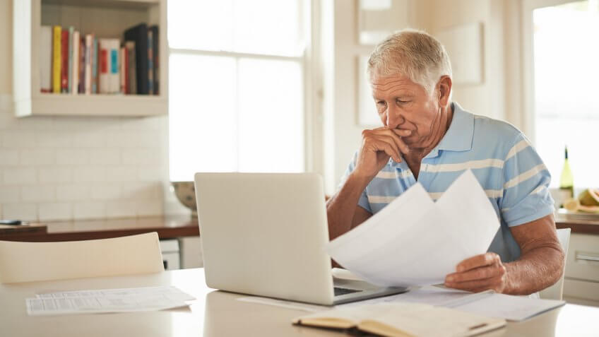 Shot of a senior man looking stressed while doing the household finances on a laptop in his kitchen.