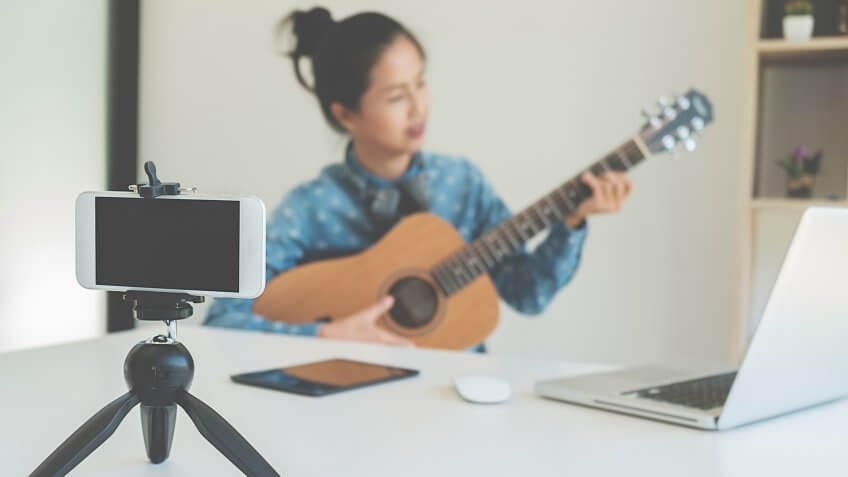 Young female blogger with smartphone recording video at home.
