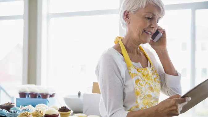 Woman on cell phone baking cupcakes in kitchen.