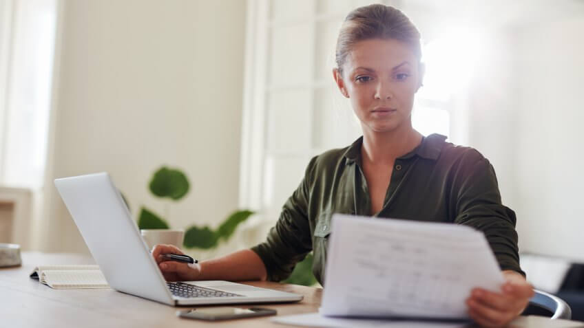 young woman sitting at table with laptop and reading documents