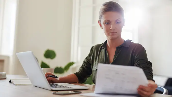 young woman sitting at table with laptop and reading documents