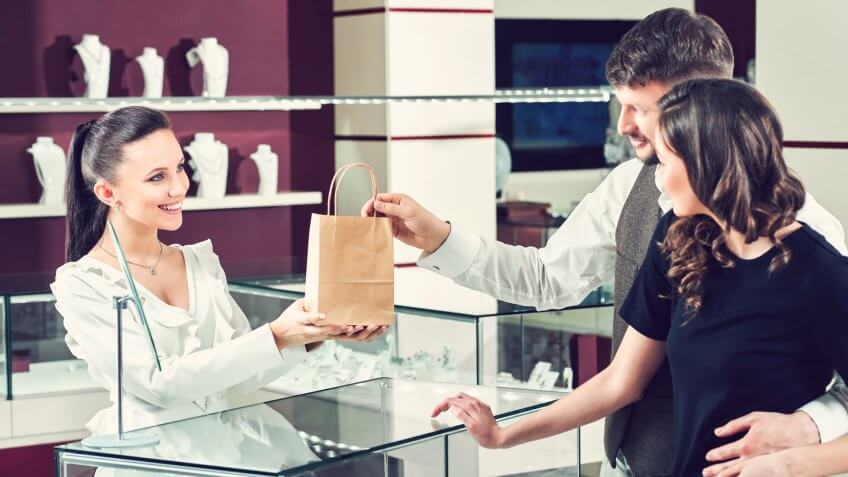 Cheerful female jeweler handing purchase in a shopping bag to he.