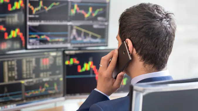 Over the shoulder view of and stock broker trading online while accepting orders by phone.
