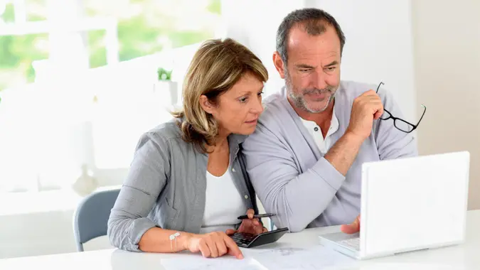 Couple reading construction plan at home with use of laptop.