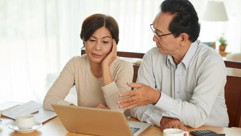 Unhappy Vietnamese senior couple discussing family budget.