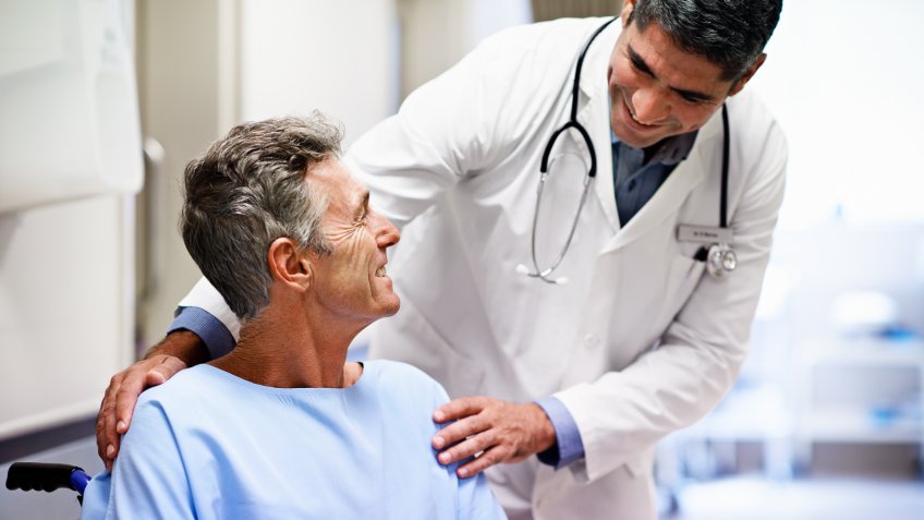 Shot of a doctor talking to a patient in a wheelchair in a hospital corridor.