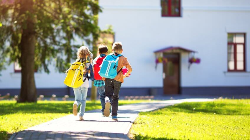 Children with rucksacks running in the park near school.