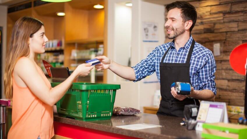 Profile view of a young woman paying with a credit card to a store clerk in a supermarket.
