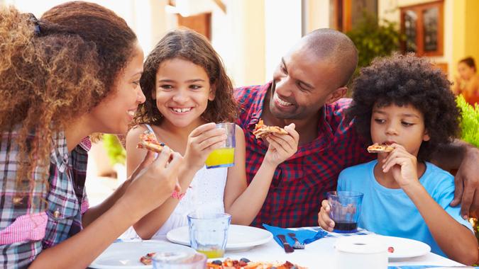 Family Eating Meal At Outdoor Restaurant Together, Smiling.