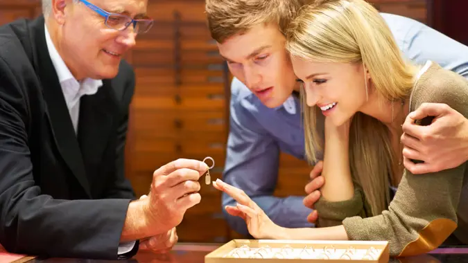 Mature jewelry store clerk assisting a couple in choosing an engagement ring.