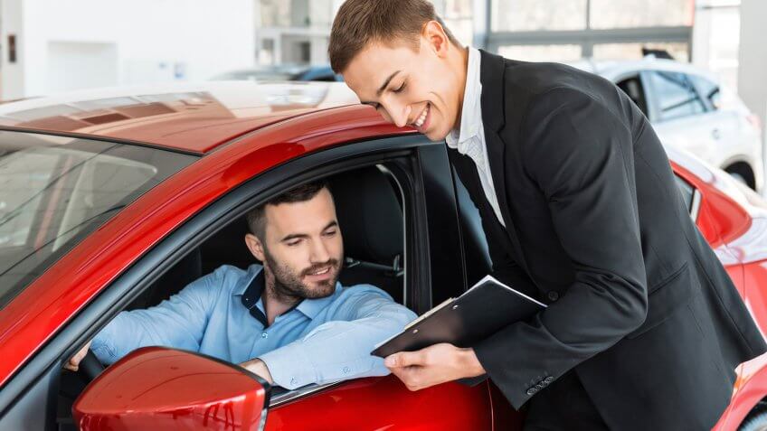 Photo of young male consultant and buyer signing contract for new car in auto show.