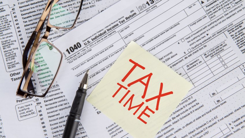 CLoseup of a text of tax time on the paper note with tax form, glasses, and pen.