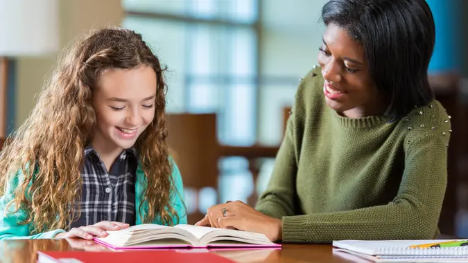 College age African American student volunteering during after school program, tutoring elementary student with reading and math homework.