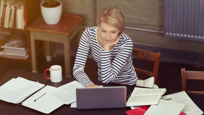 Attractive businesswoman surrounded by paperwork as she sits at her desk working on a laptop computer, high angle view.