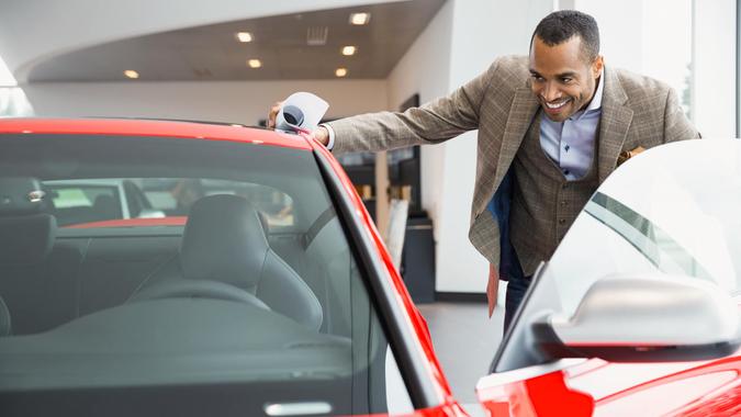 Man looking inside car in car dealership showroom.