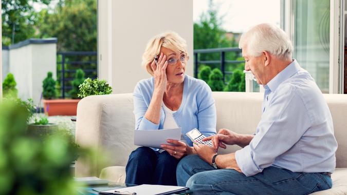 Worried senior couple sitting on sofa at home and looking over bills.