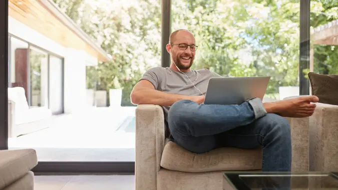 Indoor shot of a happy mature man having video call with laptop and earphones while sitting on the couch at home.
