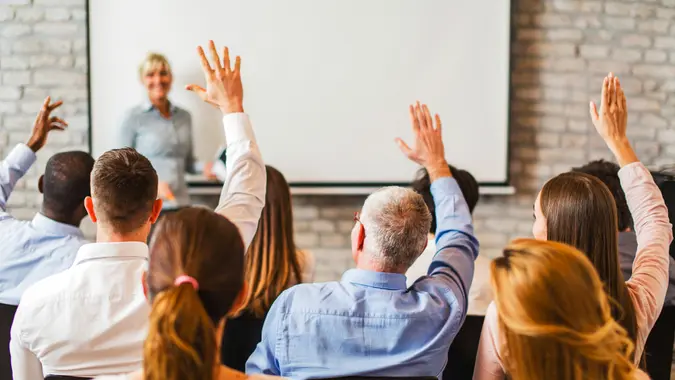 Rear view of group of business people at a lecture raising their hand ready to answer the question.