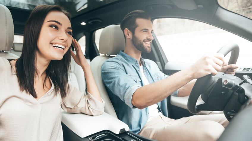 Beautiful young couple sitting on the front passenger seats and smiling while handsome man driving a car.