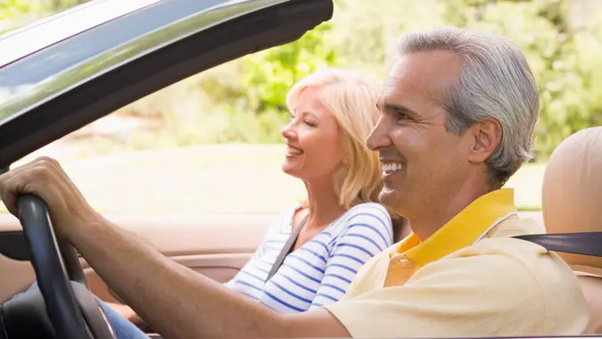 Couple driving in convertible car with top down smiling.
