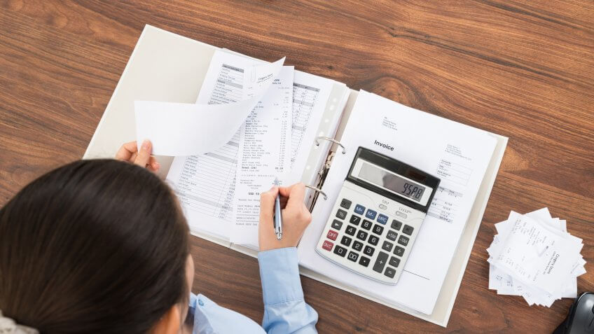 Businesswoman Calculating Tax At Desk With Calculator In Office.