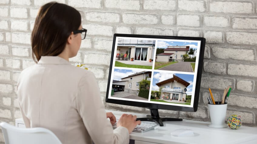 Rear View Of A Businesswoman Looking At House Photos On Computer In Office.