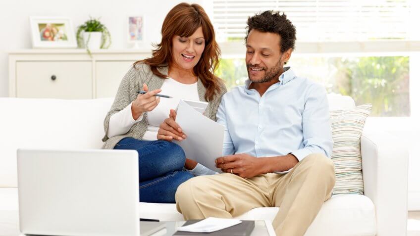 Portrait of interracial couple sitting together on sofa calculating monthly expenses - The pictures on the dresser or window or side board belong to the photographer.