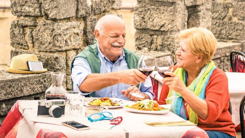 Senior couple having fun and eating at restaurant during travel - Mature man and woman wife in old city town bar during active elderly vacation - Happy retirement concept with retired people together.